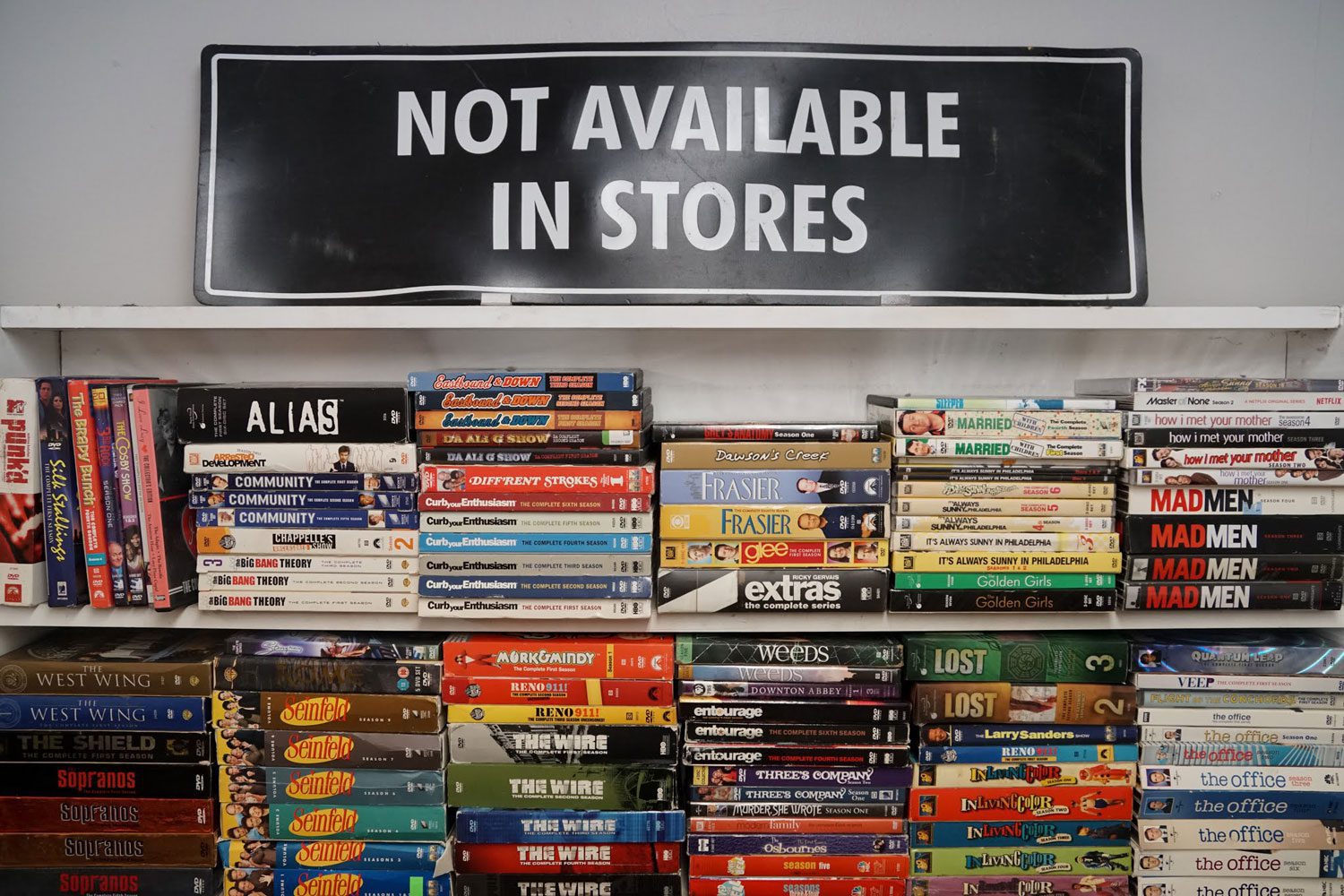 stocked shelves of videos and dvds with "Not Available In Stores" sign